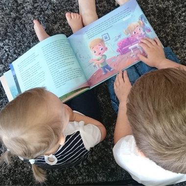 Dzieci czytające książkę z ilustracjami na dywanie